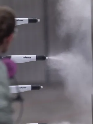 Industrial spray painting process with a worker and multiple nozzles spraying paint on metal panels