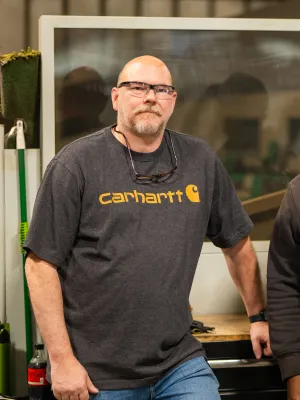 Two men wearing Carhartt clothing standing in a workshop with safety glasses and casual workwear.