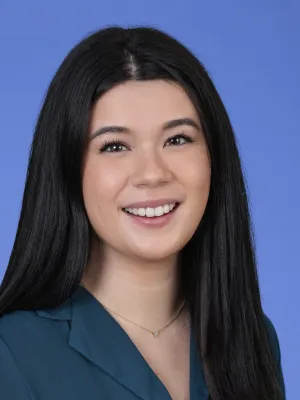 Smiling young woman with long black hair wearing a teal blouse and a delicate necklace on a blue background