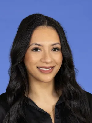 Smiling woman with long dark hair wearing a black blouse against a blue background