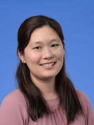 Smiling woman with long dark hair wearing a mauve blouse against a solid blue background