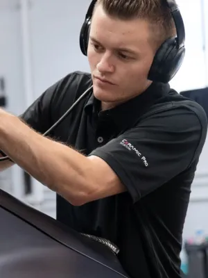 A professional detailing technician polishes a car using a high-speed buffer in a modern workshop setting.