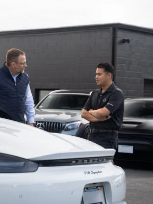 Two men discussing a white convertible sports car at a dealership, surrounded by luxury vehicles.