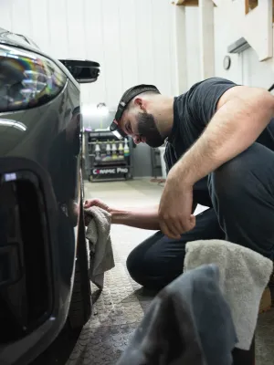 A man carefully detailing a car tire with a cloth in a bright garage setting.