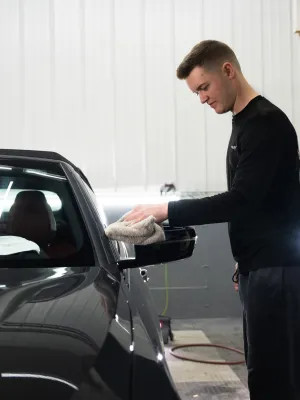 A young man detailing a car in a well-lit garage, focused on cleaning the vehicle's exterior.