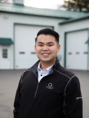 Smiling professional man in a black jacket stands outside a modern building with garage doors.