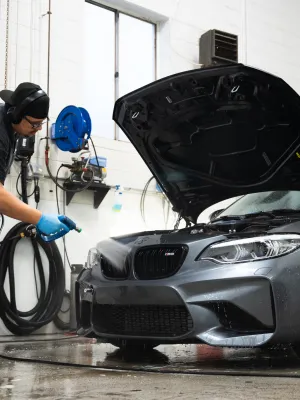 A technician washing a BMW M2 sports car in a clean garage with tools nearby.