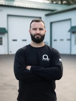 Confident man with a beard wearing a black long-sleeve shirt, standing in front of a garage.