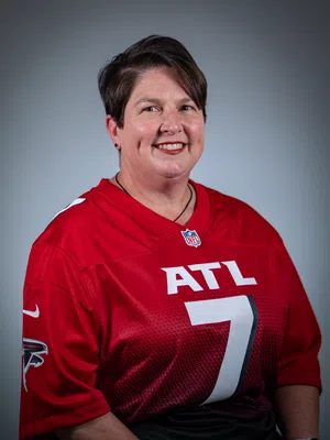 Smiling woman wearing red Atlanta Falcons NFL jersey with number 7 on gray background.