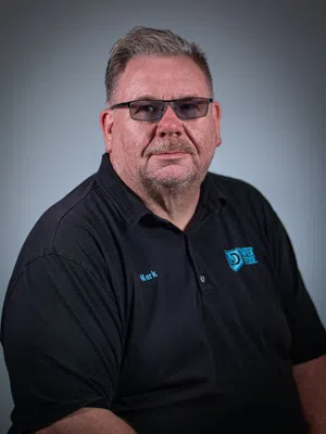 Middle-aged man with mustache wearing a gray polo shirt with company logo on a gray background.