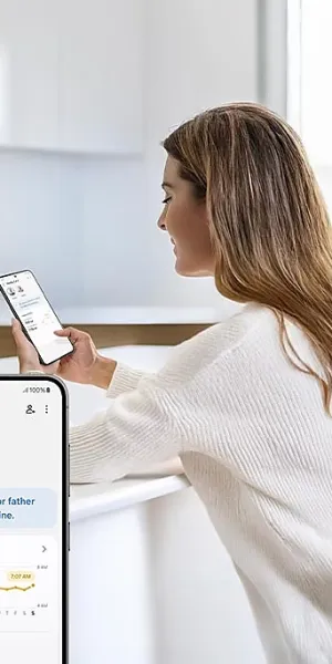 Woman in white sweater using a smartphone displaying a family care app reminding medicine times and activity logs