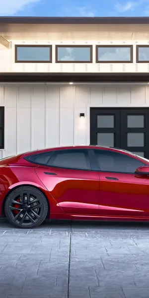 Red electric car charging outside a modern white house with black windows and garage door on a sunny day