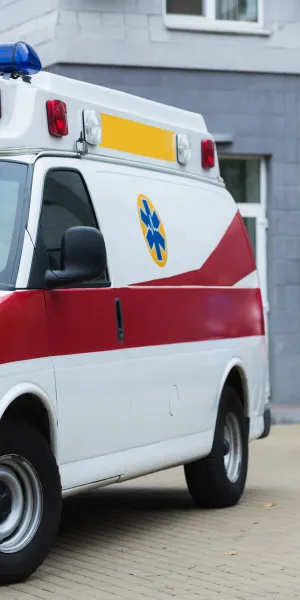 White and red ambulance parked outside a building with medical staff conversing nearby in uniforms.