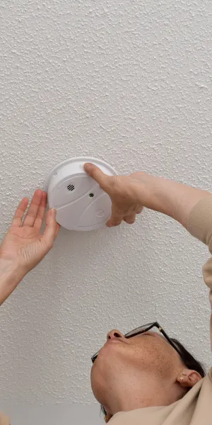 Person testing or installing a smoke detector on a textured white ceiling for safety.