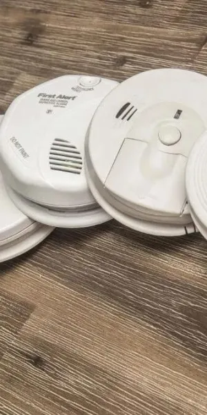 Various white smoke and carbon monoxide detectors arranged on a wooden floor showcasing different designs and features.