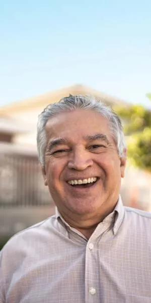 Smiling elderly man with gray hair wearing a light-colored button-up shirt outdoors on a sunny day