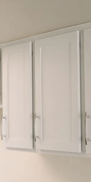 Modern white kitchen cabinets with silver handles mounted on beige wall under ceiling lighting