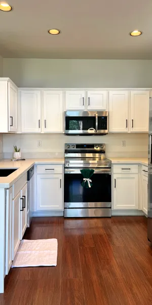 Modern kitchen with white cabinets, stainless steel appliances, dark wood floor, and black faucet with sink.
