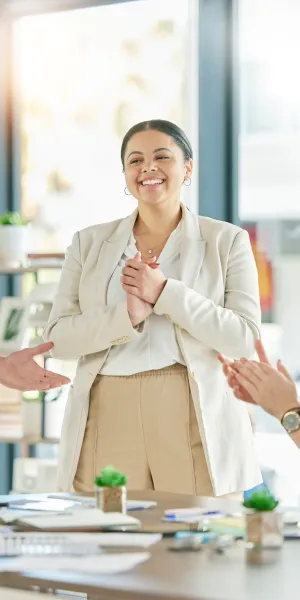Smiling businesswoman receiving applause from colleagues during a meeting in a modern office.