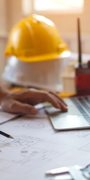 Engineer working on architectural blueprints with laptop, safety helmet, and walkie-talkie on desk in office
