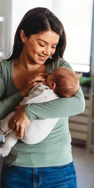 Young mother in green top lovingly holding and smiling at her baby in a cozy modern living room.