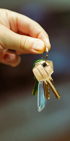 Hand holding a set of keys with multiple metal keys on a keyring over a blurred background