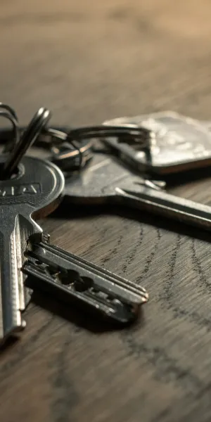 Metal keys on a keyring resting on a wooden surface with natural light and shadows.