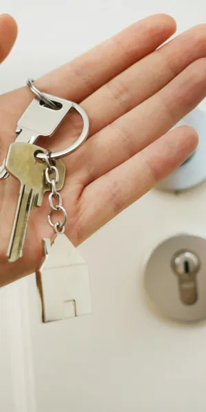 Hand holding house key with keychain near a door lock symbolizing home ownership or new house