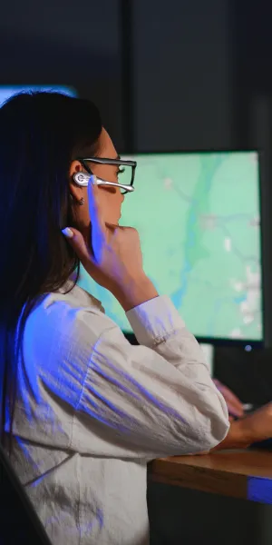 Two people with headsets monitoring maps on computer screens in a control center environment.