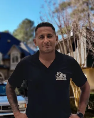 Man in Joe's Roofing shirt stands confidently in front of a large house and roofing service van on a sunny day