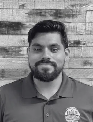 Bearded man wearing a collared shirt with a company logo, smiling in front of a wooden panel wall.