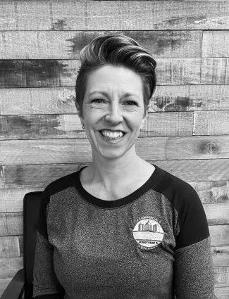 Smiling woman with short hair wearing a commercial building company shirt sitting against a wooden wall