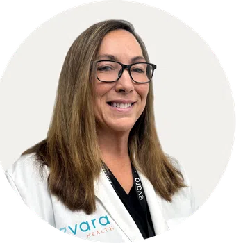 Smiling female healthcare professional wearing glasses and white coat with Evara Health logo on it