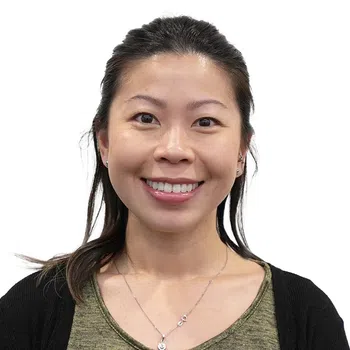 Smiling Asian woman with long hair wearing a green top and black cardigan against white background