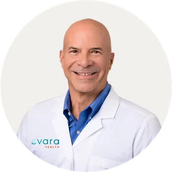 Smiling bald male doctor in white coat with blue shirt against white background