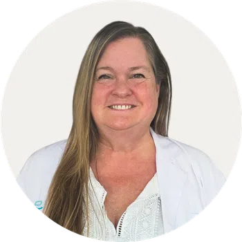 Smiling woman with long hair wearing a white lab coat and white blouse against a plain background