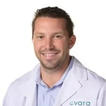 Smiling male healthcare professional wearing a white lab coat with Evara Health logo on chest.