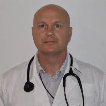 Portrait of a bald male doctor wearing a white coat and stethoscope against a plain background