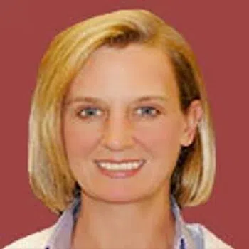 Portrait of a smiling woman with short blonde hair against a solid maroon background.