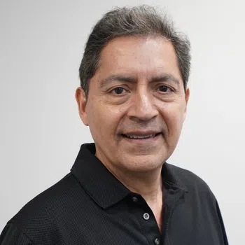 Smiling middle-aged man with short salt-and-pepper hair wearing a black polo shirt against a plain background