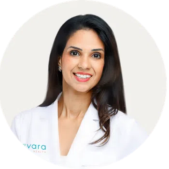 Smiling female doctor with long dark hair wearing a white medical coat against a white background