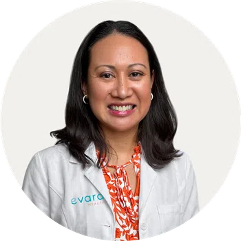 Smiling female healthcare professional wearing a white coat and orange floral blouse against a white background