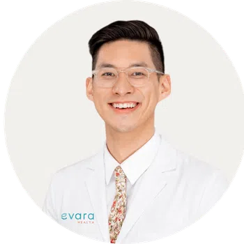 Smiling male healthcare professional wearing glasses and white coat with floral tie on white background.