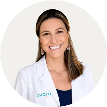 Smiling woman in a white medical coat with Evara Health logo on a white background.