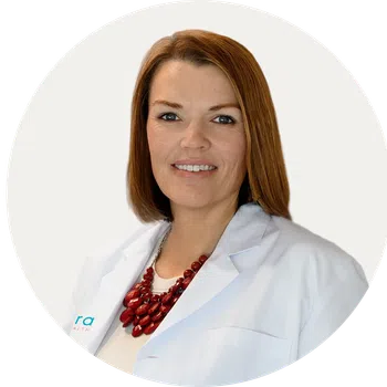 Professional woman with red hair wearing a white lab coat and red necklace on a white background.