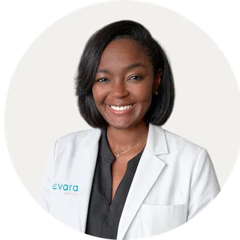 Professional smiling female healthcare worker wearing a white coat with Evara Health logo on it