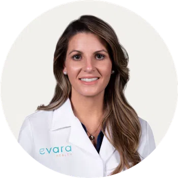 Smiling female healthcare professional with long hair wearing a white lab coat with Evara Health logo