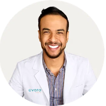 Smiling male doctor wearing a white lab coat over black scrubs against a white background