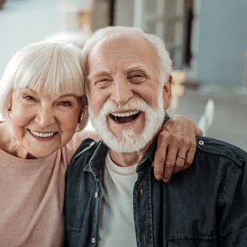 Happy elderly couple smiling outdoors with arm around each other, showing warmth and companionship.