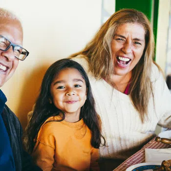 Joyful multigenerational family laughing together at a meal indoors with warm natural light and cozy atmosphere